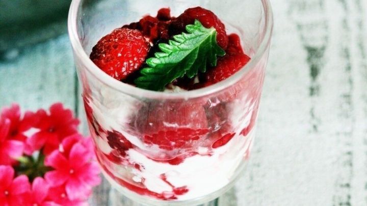 Ein Glas mit Wei&szlig;weincreme ist mit Himbeeren und frischer Minze dekoriert, umgeben von einem rustikalen Holzuntergrund.