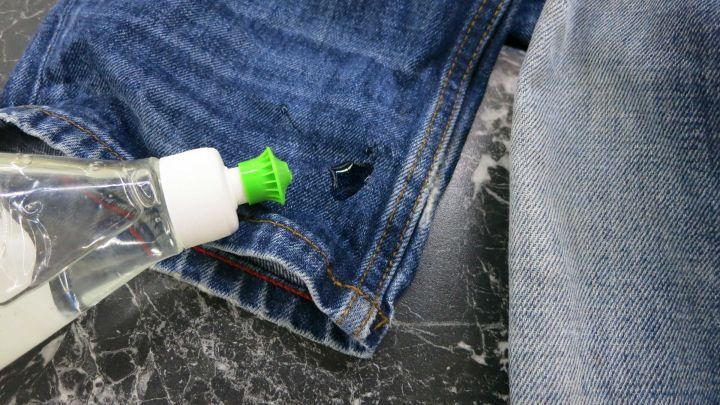 Eine Flasche Sp&uuml;lmittel steht auf dem Hosenbein einer Jeans, um einen &Ouml;lfleck vorzubehandeln.