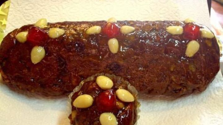 Ein l&auml;ngliches Dinkelvollkorn-Hutzelbrot liegt auf einem wei&szlig;en Papier, dekoriert mit Mandeln und roten Kirschen.