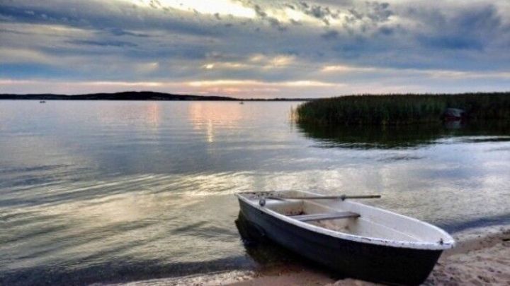 Ein Boot liegt ruhig am Ufer, w&auml;hrend die sanften Wellen im Sonnenuntergang spiegeln und eine friedliche Atmosph&auml;re schaffen.
