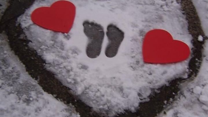 Zwei rote Herzen und Fu&szlig;abdr&uuml;cke sind in einem herzf&ouml;rmigen Bereich im Schnee platziert, umgeben von einer Schneedecke.