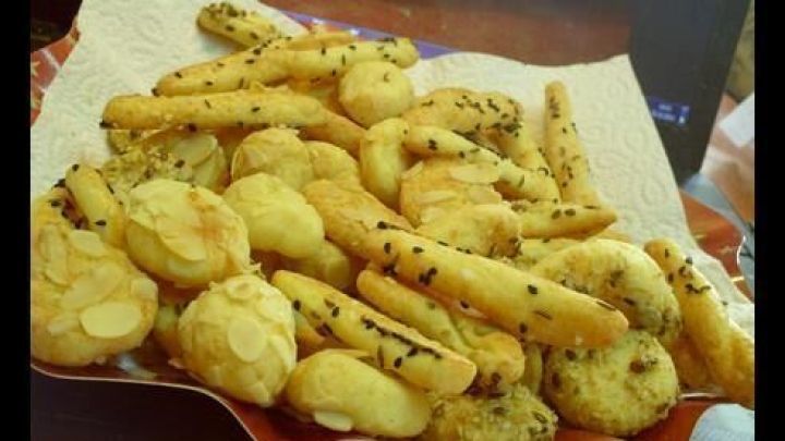 K&auml;sefours liegen knusprig auf einem Papiertuch, bestreut mit Sesam und Mandelsplittern, auf einem Teller.