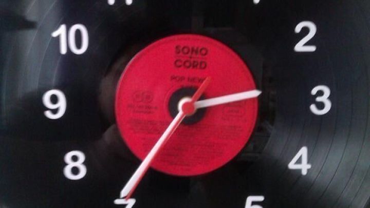 Eine Schallplatte wurde zur Uhr umfunktioniert, zeigt wei&szlig;e Zahlen von 1 bis 12 auf schwarzem Hintergrund. Im Zentrum steht "SONO CORD POP NEWS."