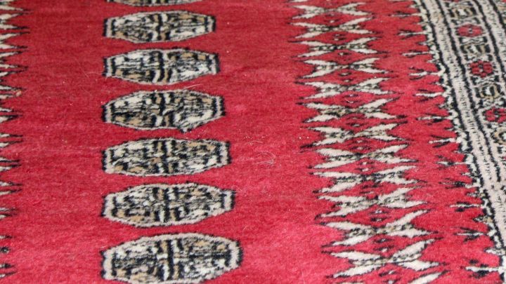 Ein roter Teppich mit grafischen Mustern zeigt einen Rotweinfleck. Der Fleck sitzt prominent auf dem Teppich.