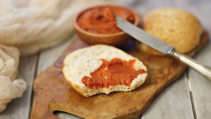 Eine belegte Br&ouml;tchenh&auml;lfte mit Tomatenbutter liegt auf einem Holzbrett, neben einer Sch&uuml;ssel mit der restlichen Butter.