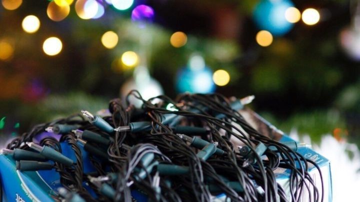 Eine Lichterkette liegt unordentlich auf einem wei&szlig;en Teppich, umgeben von einem Weihnachtsbaum mit bunten Lichtern.