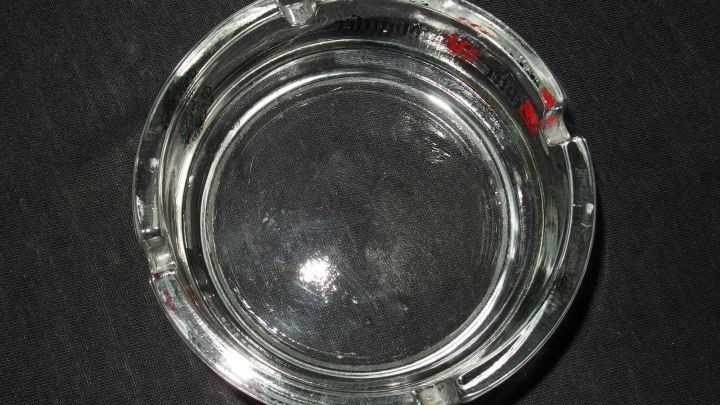 Ein dreckiger Aschenbecher liegt auf einem schwarzen Untergrund, bereit zum Reinigen und Entfernen von Abf&auml;llen.