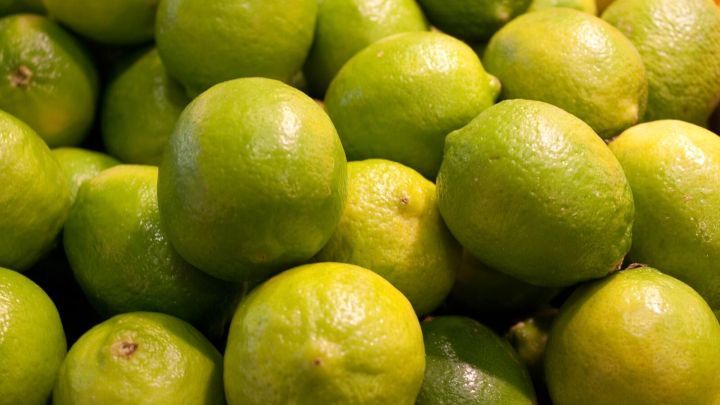 Limetten liegen &uuml;bereinander in einem Stapel; ihre gl&auml;nzende gr&uuml;ne Schale spiegelt Licht wider.