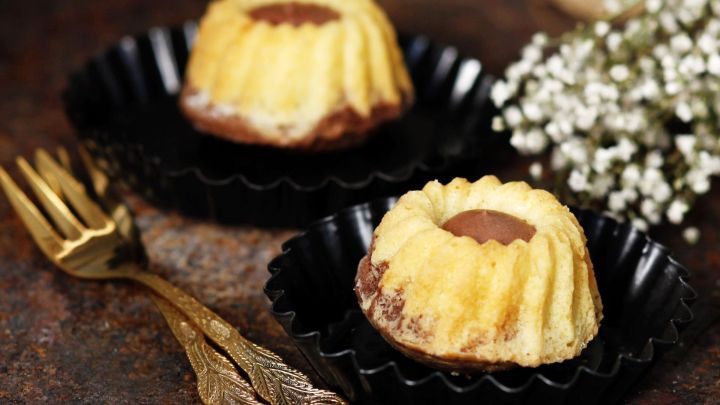 Mini-Gugelhupfe stehen auf einer rustikalen Oberfl&auml;che, h&uuml;bsch angerichtet mit einer Blume und goldenen Gabeln.