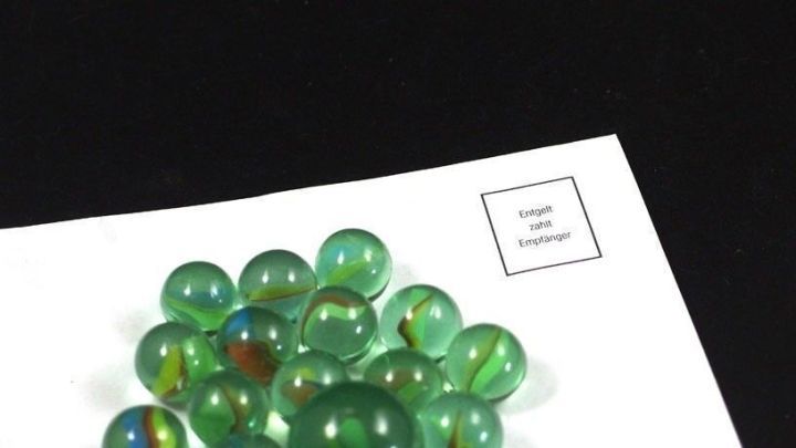 Eine Ansammlung gr&uuml;ner Murmeln liegt auf einem wei&szlig;en Blatt Papier, das auf einem schwarzen Hintergrund platziert ist.