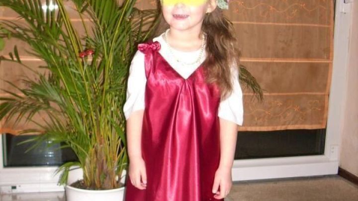 Ein Kind tr&auml;gt ein Dornr&ouml;schen-Faschingskost&uuml;m: ein langes rotes Kleid und eine Blumenkronen, steht vor Pflanzen im Wohnzimmer.