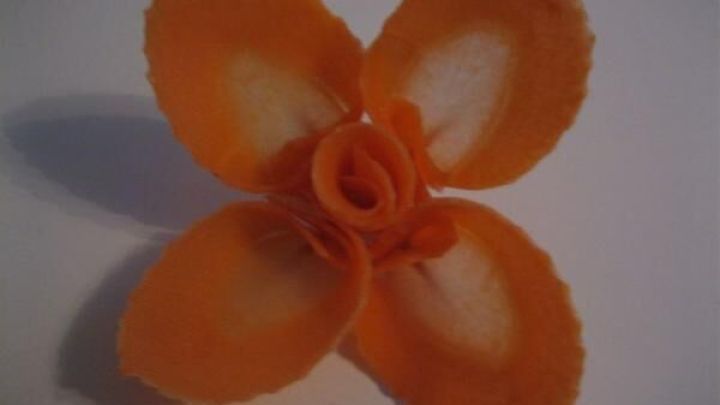 Eine leuchtend orange Dekobl&uuml;te aus einer M&ouml;hre liegt auf einem wei&szlig;en Hintergrund und zeigt kunstvoll geformte Bl&uuml;tenbl&auml;tter.