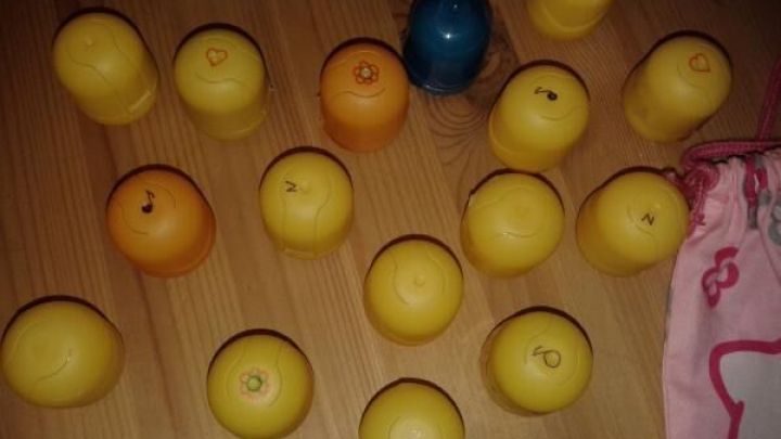 Gelbe und orange Memory-Eier mit Blumen- und Notensymbolen liegen durcheinander auf einem Holztisch neben einer rosa Tasche.