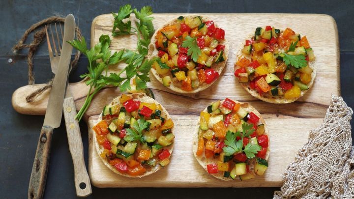 Drei knusprige Kartoffelpuffer sind mit buntem, frischem Gem&uuml;se belegt und auf einem Holzbrett angerichtet.