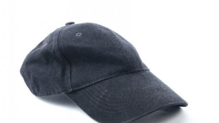 Eine dunkle Schildm&uuml;tze liegt auf einer wei&szlig;en Oberfl&auml;che, leicht nach rechts geneigt, in ruhiger Umgebung ohne Text.