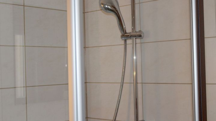 Eine Dusche mit gl&auml;nzender Armatur steht in einem hellen Badezimmer; der Essigreiniger wird zur Reinigung spr&uuml;ht.