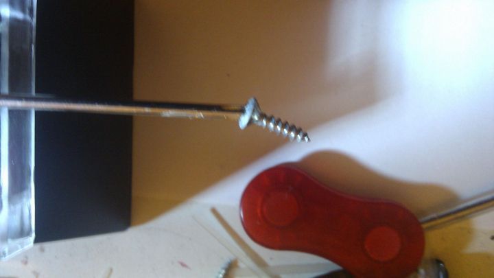 Ein l&auml;nglicher Schraubenzieher h&auml;lt eine Schraube senkrecht, umgeben von einem wei&szlig;en Untergrund und einem roten Magneten.