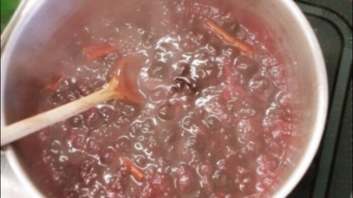 In einem Topf kochen Zimtkirschen mit einer Holzl&ouml;ffel, w&auml;hrend Dampf aus dem sprudelnden Wasser aufsteigt.