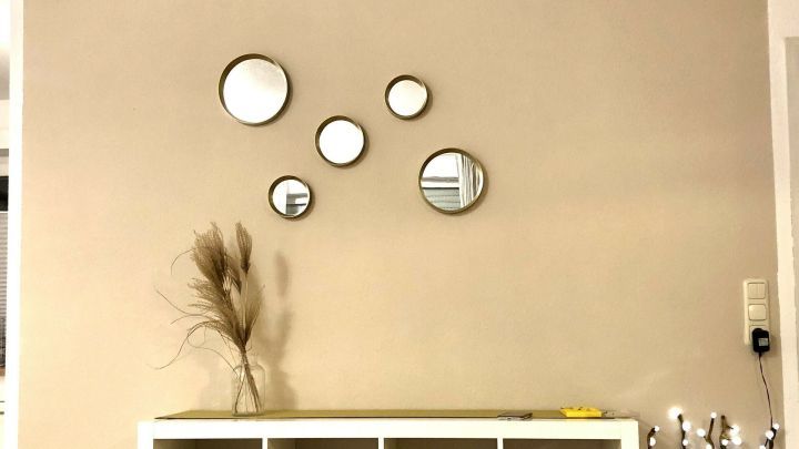 Eine decorierte Wand zeigt mehrere Spiegel, die an einem hellbeigen Hintergrund h&auml;ngen, um einen modernen Raum zu versch&ouml;nern.