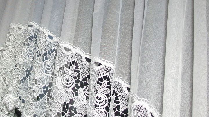 Wei&szlig;e Gardinen mit zarten Spitzen stehen senkrecht und filtern das Licht in einem hellen Raum.