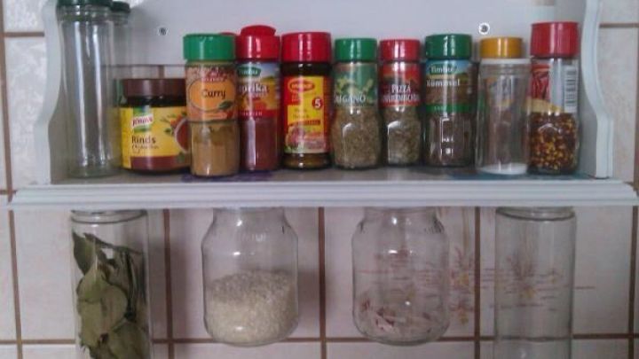 Vollgestelltes Gew&uuml;rzregal mit verschiedenen Gew&uuml;rzdosen und darunter h&auml;ngenden Gl&auml;sern an gefliester K&uuml;chenwand.