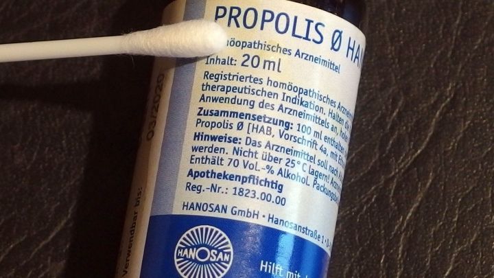 Ein Fl&auml;schchen mit Propolis steht auf einer dunklen Oberfl&auml;che, w&auml;hrend ein Wattest&auml;bchen das Mittel aufnimmt.