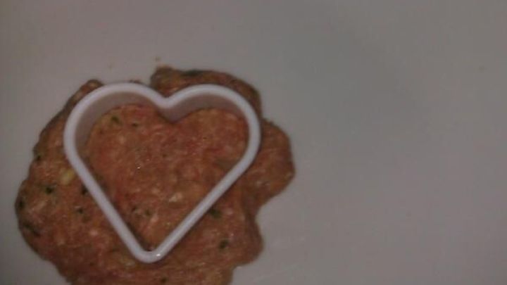 Eine Frikadelle wird auf einem Teller geformt, mithilfe eines herzf&ouml;rmigen Ausstechers, umgeben von wei&szlig;em Hintergrund.