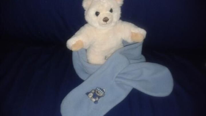 Ein Kuscheltier sitzt auf einem blauen Untergrund, umgeben von blauen Socken, die Kinderkleidung repr&auml;sentieren.