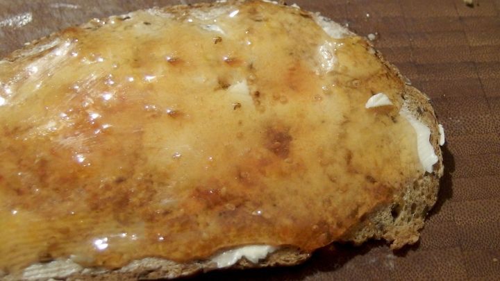 Ein knuspriges St&uuml;ck Brot ist mit goldenem Weingelee &uuml;berzogen und liegt auf einem Holzbrett.