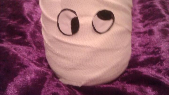 Ein Teelichtglas, umwickelt mit wei&szlig;em Stoff wie eine Mumie, steht auf einem lila Tuch und hat witzige Augen angebracht.