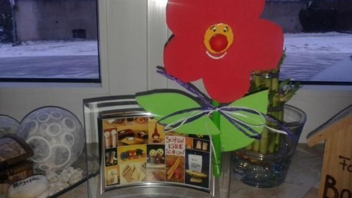 Eine bunte Kochl&ouml;ffel-Blume steht in einem Fenster, umgeben von Deko, und strahlt Freude in den Raum aus.