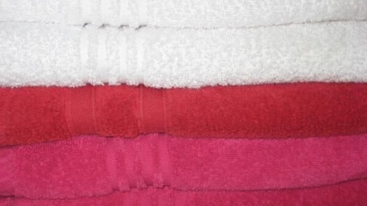 Gefaltete Handt&uuml;cher in Wei&szlig;, Rot und Pink liegen aufeinandergestapelt, symbolisierend saubere Kochw&auml;sche im Regal.