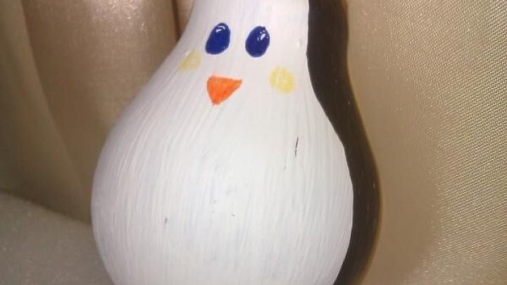Ein dekorativer Pinguin aus einer Gl&uuml;hbirne sitzt auf einem hellen Untergrund und strahlt winterliche Stimmung aus.