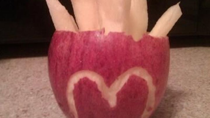 Apfelst&uuml;ckchen, geschnitten wie Pommes, stecken in einer roten Apfelh&auml;lfte mit M-F&ouml;rmung, auf einer K&uuml;chenplatte.