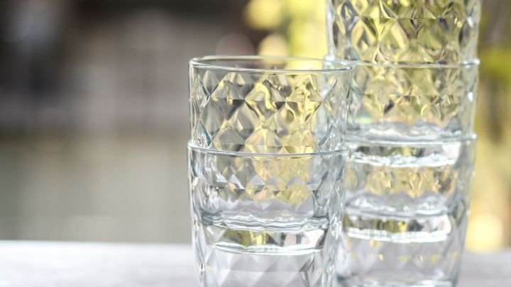 Klar gl&auml;nzende Gl&auml;ser stehen gestapelt auf einem Tisch, umgeben von einer unscharfen, nat&uuml;rlichen Kulisse.