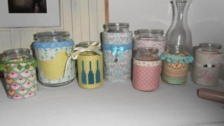 Gl&auml;ser sind kreativ mit bunten Stoffresten dekoriert und auf einem Tisch in einem hellen Raum angeordnet.