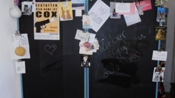 Eine Raumteilerwand dient als Pinn- und Tafelwand. Darauf sind Notizzettel, Karten und Kreidetext &bdquo;dieter guys on alle tutis&rdquo; zu sehen.