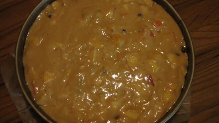 Eine gef&uuml;llte Apfel-Mandel-Nuss-Torte liegt in einer runden Backform auf einem Holzuntergrund, bereit zum Backen.