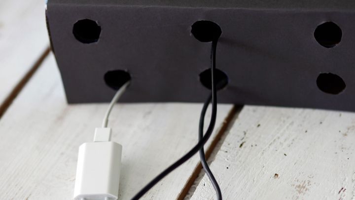 Ein Kabeldiener aus einer Capri-Sun Box mit Kabeln, die durch L&ouml;cher f&uuml;r Ordnung in einem schlichten Raum verlaufen.