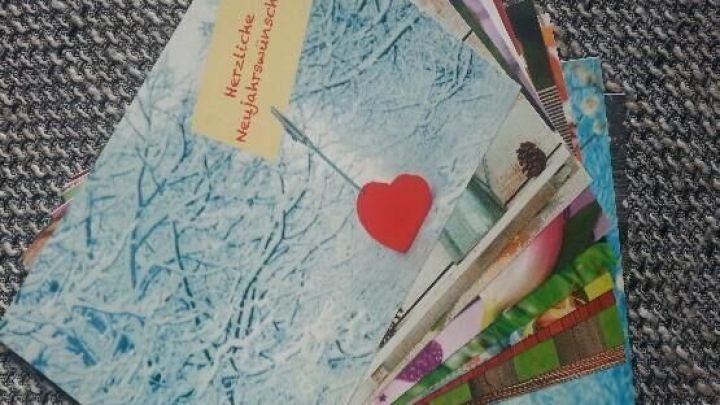 Bunte Postkarten liegen auf einem grauen Untergrund, einige zeigen winterliche Motive und Herzen.