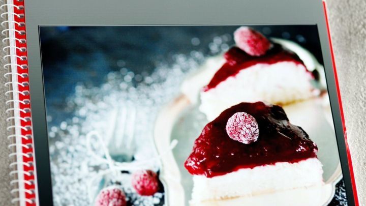 Ein Rezeptbuch zeigt ein verf&uuml;hrerisches Dessert mit Himbeeren, angerichtet auf einem Teller, umgeben von Puderzucker.