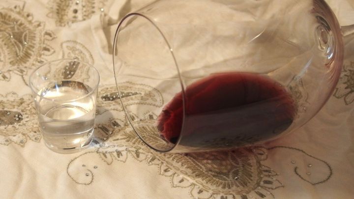 Ein umgefallener Weinglas mit Rotwein steht neben einem Schnapsglas auf einer eleganten Tischdecke.