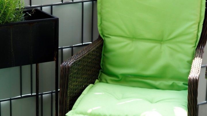 Ein gr&uuml;nes Polster sitzt auf einem Rattanstuhl, w&auml;hrend es in einem modernen Au&szlig;enbereich neben einer Pflanze steht.