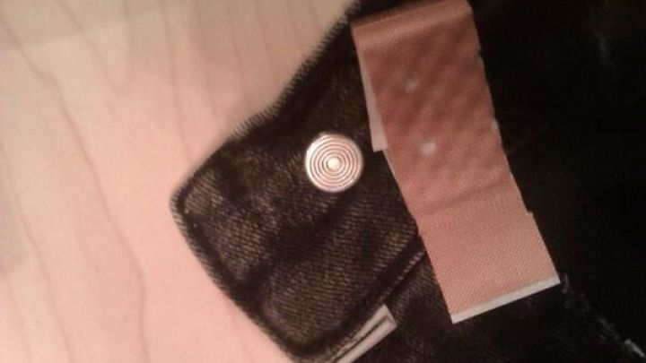 Ein Hosenknopf aus Nickel ist mit einem Pflaster abgedeckt. Die Jeans liegt auf einem Holztisch.