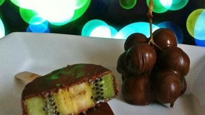 Ein Schoko-Kiwi Lutscher liegt auf einem Teller, w&auml;hrend bunte Lichter im Hintergrund leuchten, die ein festliches Ambiente schaffen.