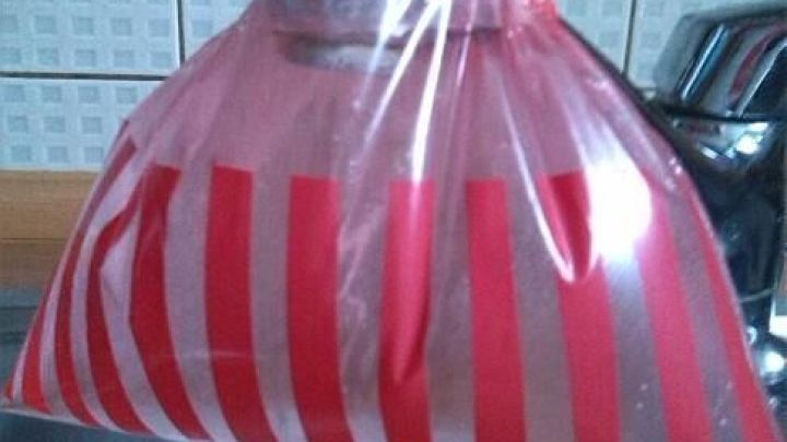 Ein Wasserhahn ist mit einem rot gestreiften Beutel umh&uuml;llt, um den Perlator zu entkalken, &uuml;ber einer Sp&uuml;le in einer K&uuml;che.