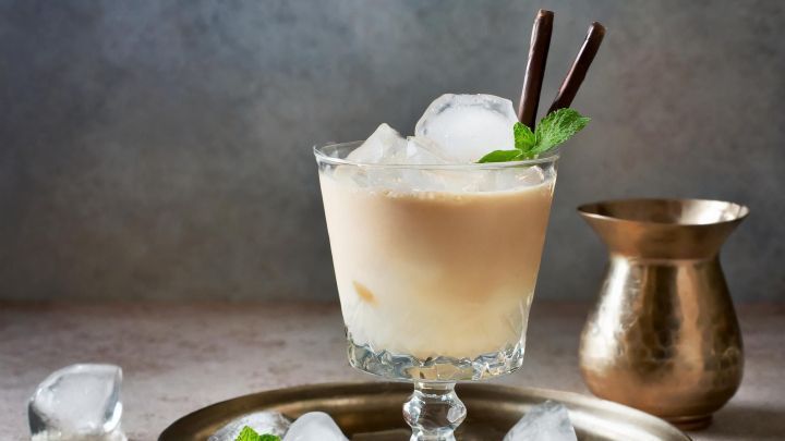 Ein elegantes Getr&auml;nk im Glas mit Eisw&uuml;rfeln, garniert mit Minze und Schokoladenstiften auf einem Silbertablett.