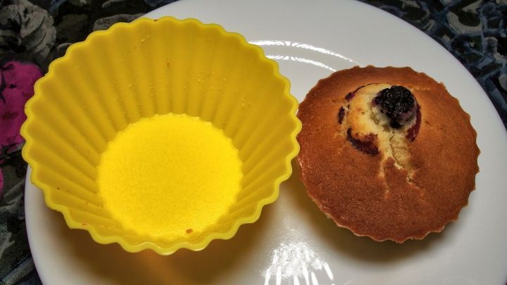 Eine gelbe Silikonform steht neben einem Muffin auf einem Teller, der fertig gebacken und leicht angebrannt aussieht.