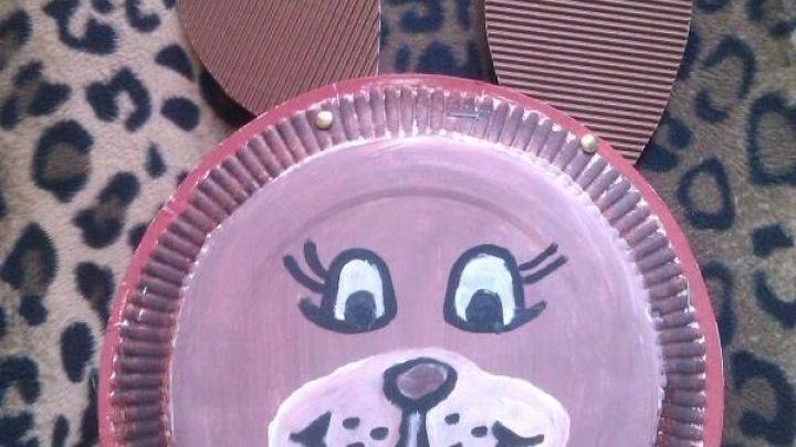 Papier-Osterhase aus bemaltem Teller mit Pappohren auf Leopardenmuster-Decke liegend.