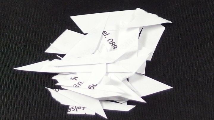 Zerknitterte, unsortierte Papierschnipsel liegen auf einem schwarzen Untergrund, was auf unsachgem&auml;&szlig;e Briefentsorgung hindeutet.